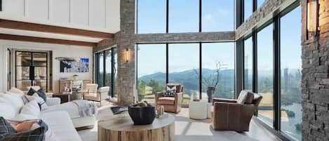 A spacious living room with a large window, a round wooden coffee table, and a view of the mountains.