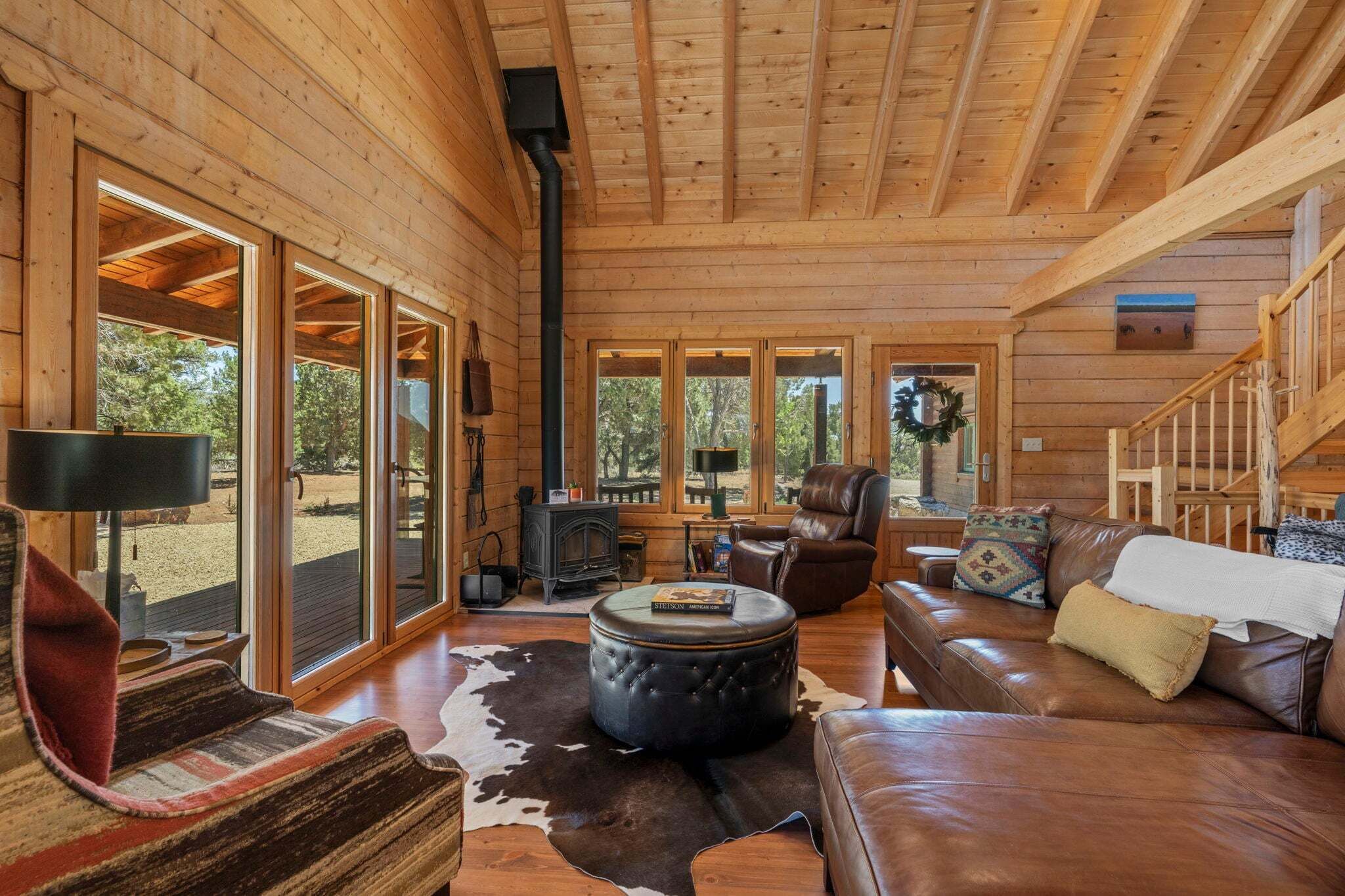L’intérieur d’une cabane en rondins, avec une cheminée, des meubles en cuir et de grandes fenêtres.