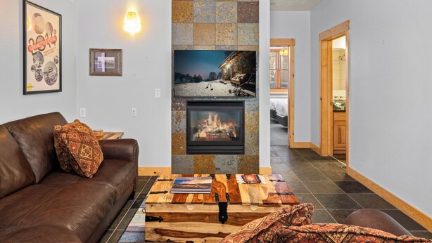 A living room with a fireplace, a brown leather couch, a coffee table, and a television mounted on the wall.