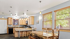 A kitchen with wooden cabinets, a granite countertop, a dining table with chairs, and a colorful striped rug.