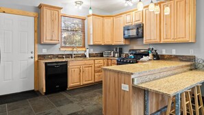A modern kitchen with wooden cabinets, granite countertops, a built-in stove, and a large island with bar stools.