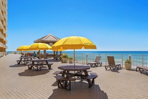 A beachside patio with yellow umbrellas, wooden tables, and lounge chairs.