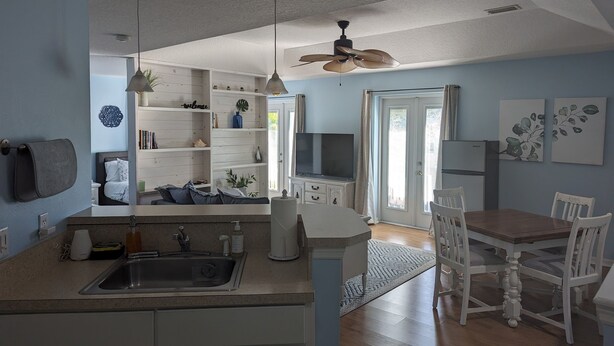 A modern kitchen with a sink, cabinets, and a dining area with white chairs and a table. - Charming Cocoa Village Hideaway (Cocoa)