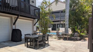 A backyard with a covered patio table, a pool, and a two-story house with a balcony. - Charming Cocoa Village Hideaway (Cocoa)