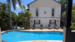 A swimming pool with lounge chairs and a house with shutters. - Charming Cocoa Village Hideaway (Cocoa)