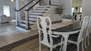 A dining area with a dark wooden table, white chairs, a woven placemat, and a chandelier. - Charming Cocoa Village Oasis (Cocoa)