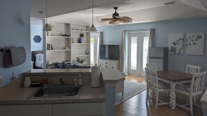 A modern kitchen with a sink, cabinets, and a dining area with white chairs and a table. - Charming Cocoa Village Oasis (Cocoa)