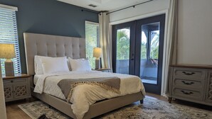A bedroom with a large bed, a nightstand, a dresser, and a view of the outdoors through a sliding glass door. - Charming Cocoa Village Oasis (Cocoa)
