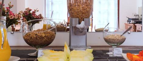 A breakfast buffet with bowls of cereal, a fruit plate, and a juice pitcher.