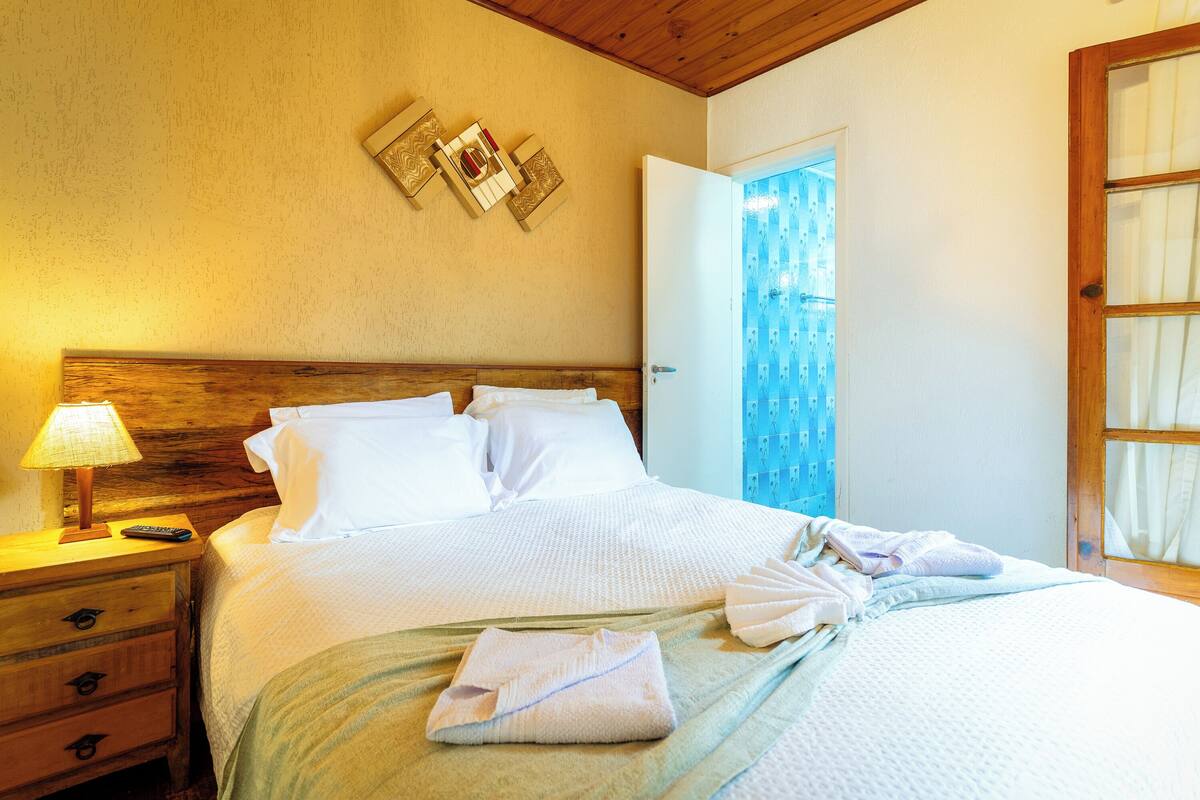 Una cama bien hecha con sábanas blancas, cabecera de madera y mesita de noche con lámpara.