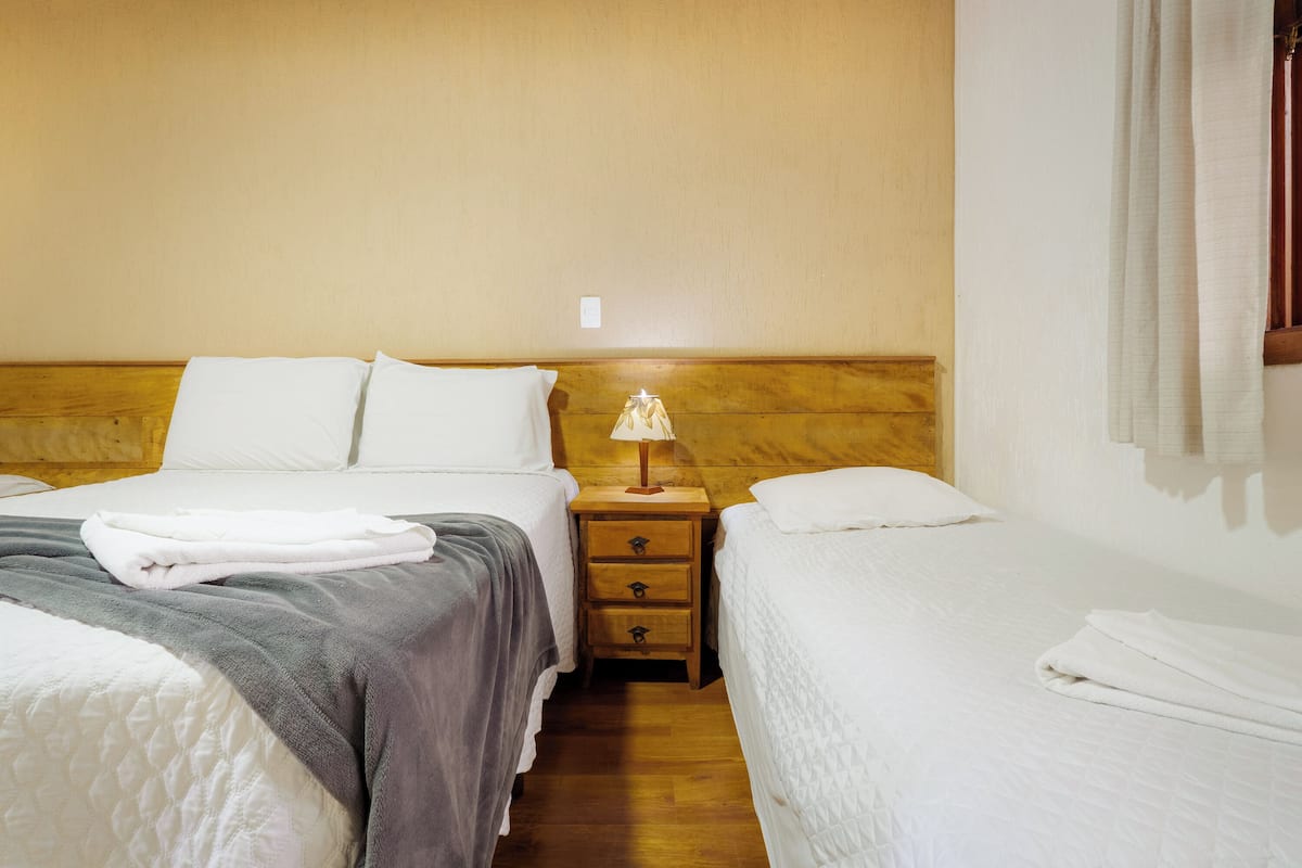 Habitación de hotel con dos camas, cabeceros de madera, una mesita de noche con lámpara y una ventana con cortinas.
