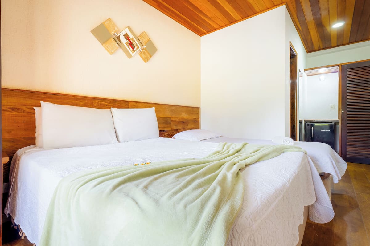 Una habitación de hotel con dos camas, cabeceros de madera, ropa de cama blanca y techo de madera.