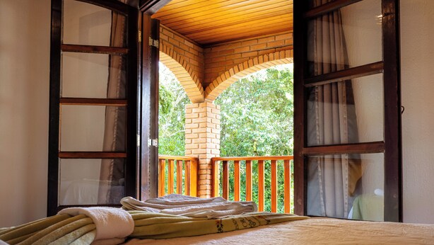 Una habitación con cama, techo de madera y vista a la vegetación por una ventana abierta.