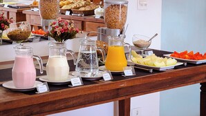 Una mesa de buffet con diversas opciones de comida y bebida, como cereales, leche, zumo y frutas.