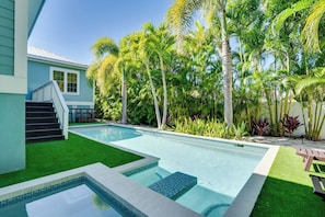 A swimming pool with a clear blue water feature, surrounded by lush greenery and palm trees.