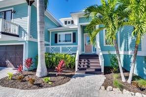 A two-story house with a front porch, a garage, and a landscaped garden with palm trees and shrubs.