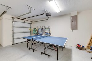 Una mesa de ping pong en una habitación con un proyector instalado en el techo y un aire acondicionado fijado a la pared.