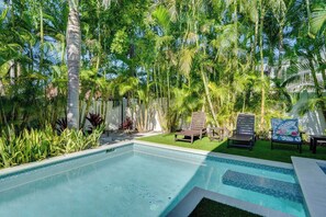 A swimming pool with a tiled edge, surrounded by lush greenery and palm trees.