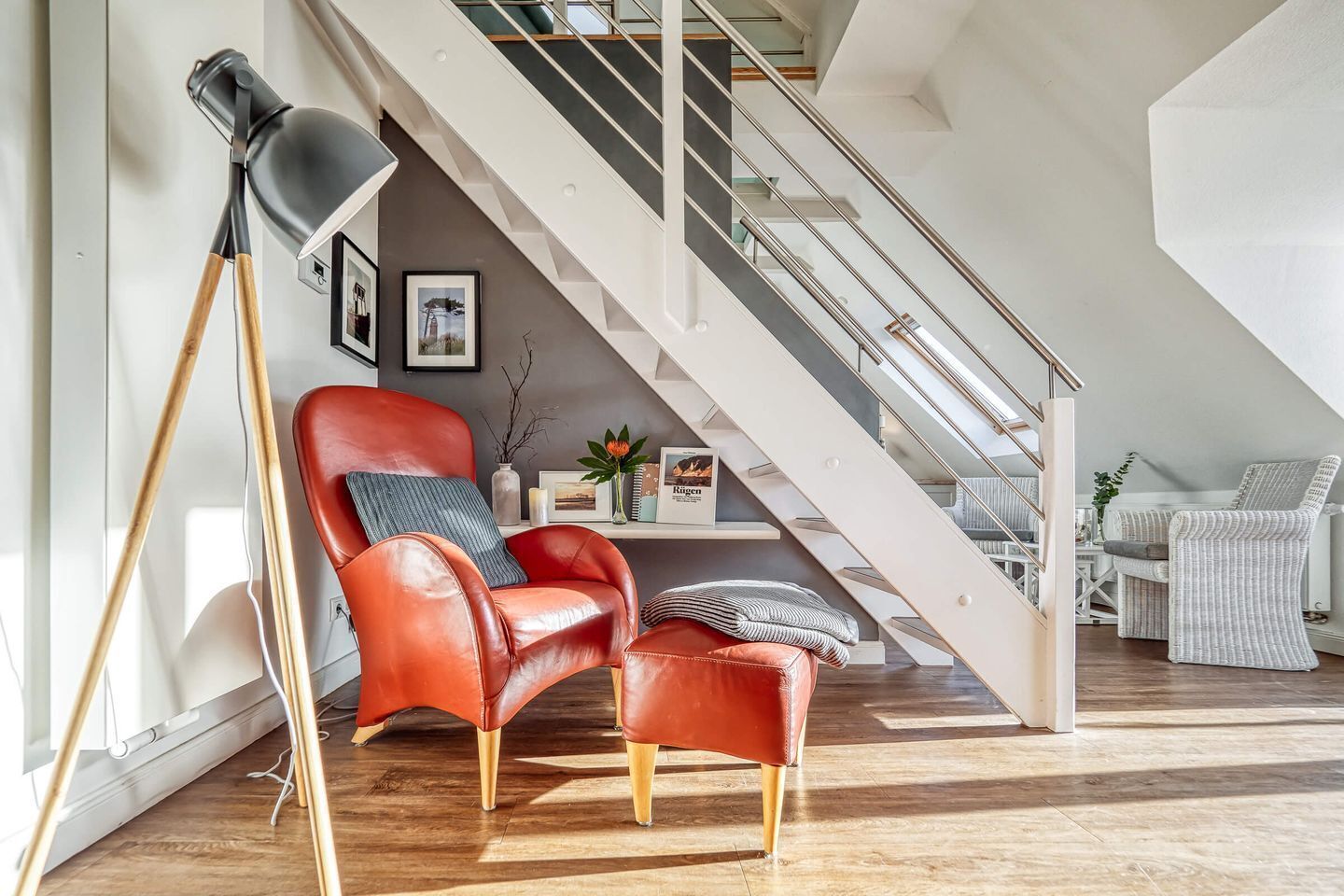 Un salon moderne avec un fauteuil en cuir rouge, une lampe sur pied et un escalier menant à un niveau supérieur.