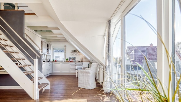 A modern loft with a curved staircase, a kitchen with white cabinets, and large windows offering a view of the neighborhood.