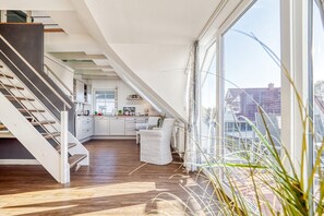 Un loft moderne doté d’un escalier à la forme arrondie, d’une cuisine avec des meubles blancs et de grandes fenêtres offrant une vue sur le quartier.
