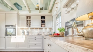A modern kitchen with white cabinetry, a wooden countertop, and a stainless steel kettle.