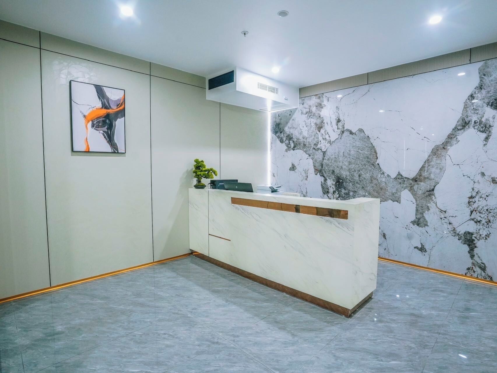 A reception area with a marble wall, a reception desk, a potted plant, and a framed abstract painting.