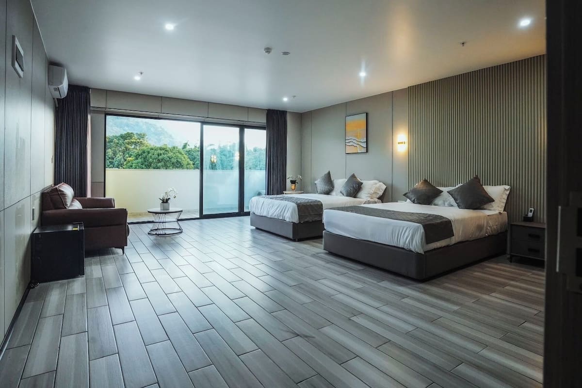 A modern bedroom with two beds, a sofa, and a balcony with a view of greenery.
