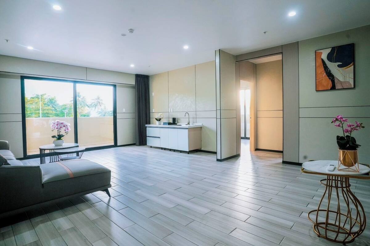 A modern living room with a sofa, a small table with a plant, and a kitchen area with a sink and cabinets.