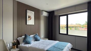 Una habitación de hotel moderna con una cama grande, una mesita redonda pequeña, una silla y un ventanal con vistas a edificios y vegetación.