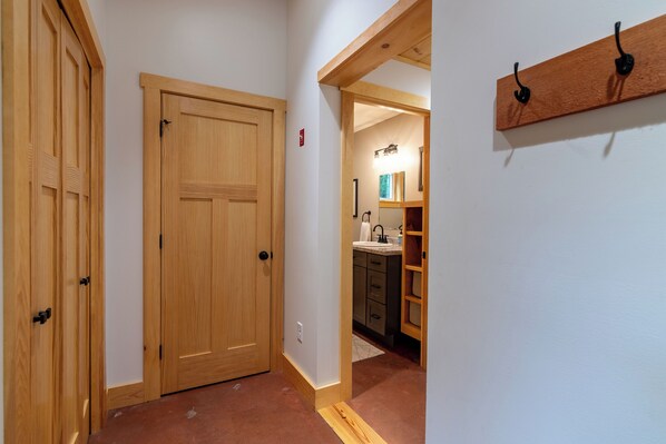 A hallway with wooden doors, a kitchen area with cabinets and a sink, and a wooden shelf with hooks.