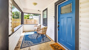 Un porche abrité avec une porte bleue, une petite table entourée de chaises et un tapis à motifs.