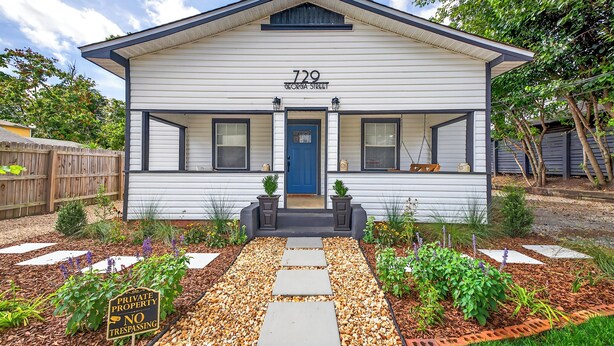 Une maison de plain-pied avec une porte bleue, portant le numéro « 729, rue Georgia », entourée d’un jardin agrémenté de pas japonais et d’un panneau indiquant « Propriété privée, entrée interdite ».