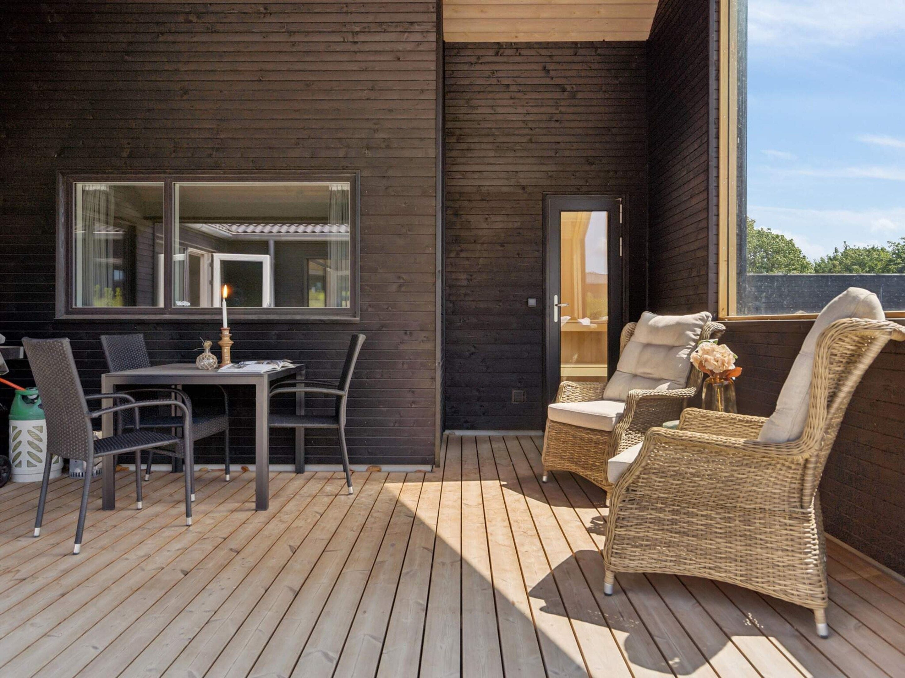 A wooden deck with a table and chairs, a wicker sofa, and a glass door leading to an interior space.