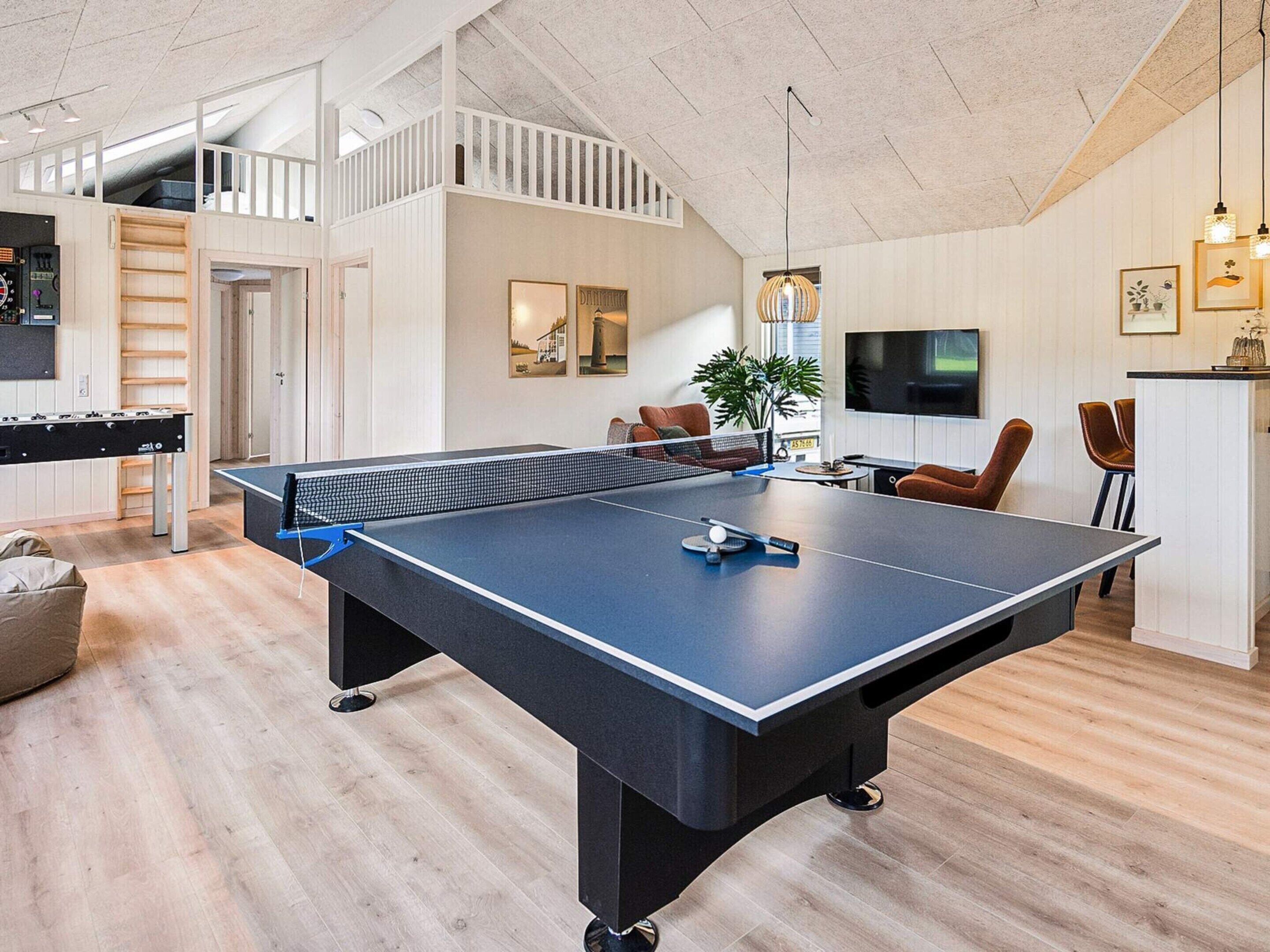 A spacious living area with a ping pong table, a foosball table, and a kitchen area with a TV and seating.