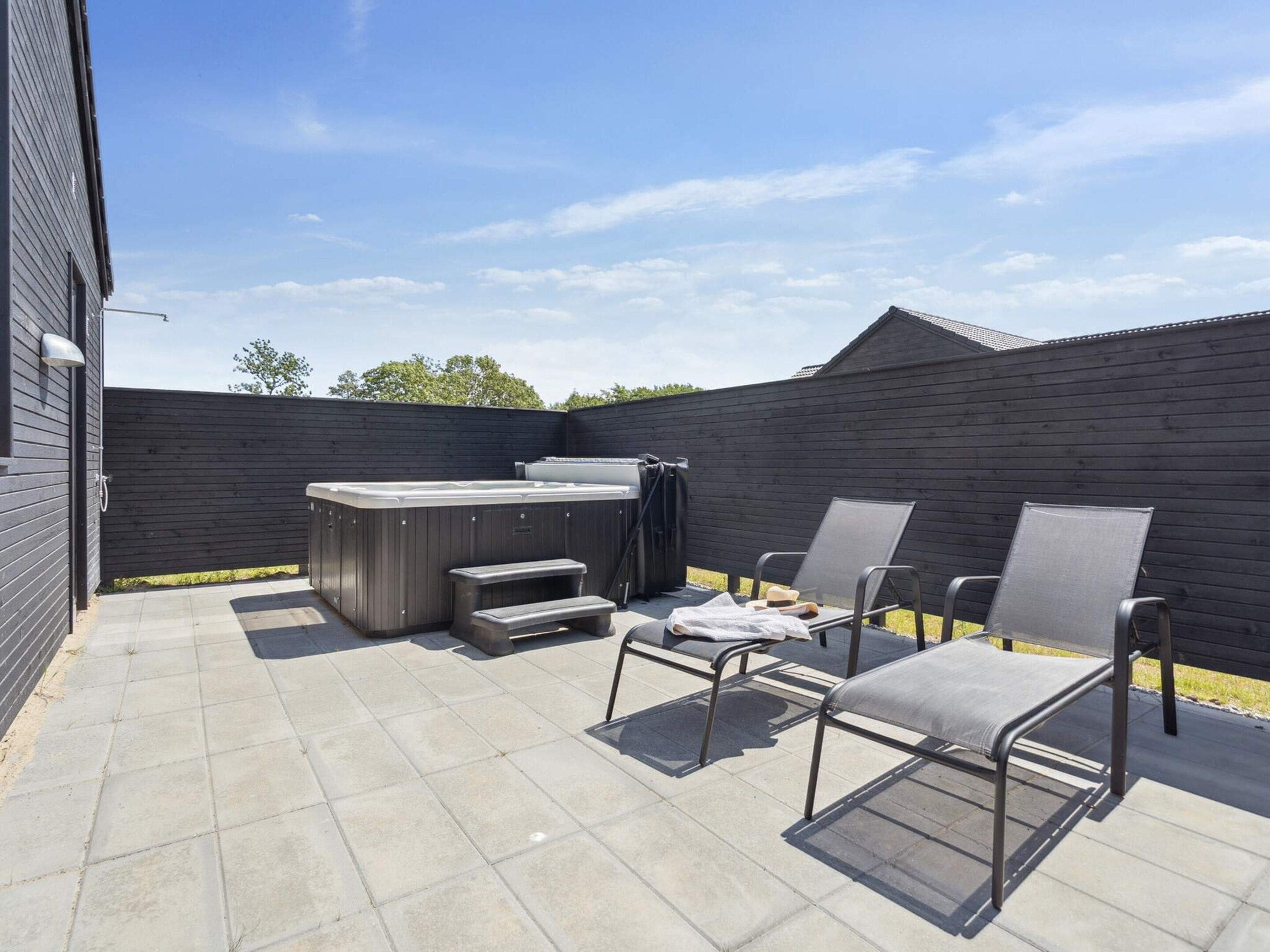 A patio with a hot tub, two chairs, and a small table.