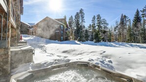 Un jacuzzi en zona exterior nevada con edificios al fondo.