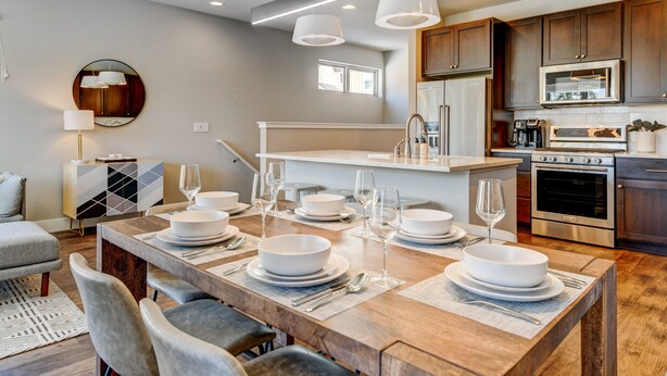 Una cocina moderna con una isla central, electrodomésticos de acero inoxidable y un comedor con una mesa de madera para cuatro.