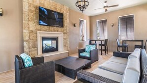 Una sala de estar moderna con una pared de piedra, una chimenea y un televisor montado encima. Hay sofás de mimbre y un comedor con una mesa y sillas.