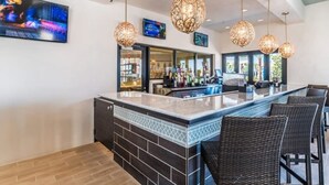 Un área de bar con una barra larga, sillas de mimbre y lámparas colgantes.