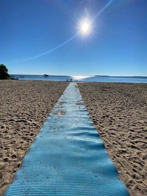 A beach with a blue mat leading to the water, clear skies, and a distant pier. - ARCA  Cozy Cabin-Innisfil Beach (Innisfil)