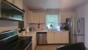 A compact kitchen with white cabinets, a stainless steel refrigerator, a microwave, a dishwasher, and a black stove. - ARCA  Cozy Cabin-Innisfil Beach (Innisfil)