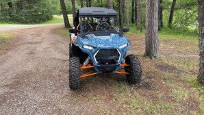 A blue Polaris ATV parked on a gravel path in a wooded area. - Lakeside Cabin "Serenity" (Town of Silver Cliff)