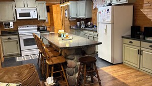 A cozy cabin-style kitchen with a stone island, wooden cabinets, and a dining area with a brown leather couch and wooden chairs. - Lakeside Cabin "Serenity" (Town of Silver Cliff)