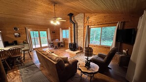 A cozy cabin interior with a fireplace, wooden furniture, and large windows offering a forest view. - Lakeside Cabin "Serenity" (Town of Silver Cliff)