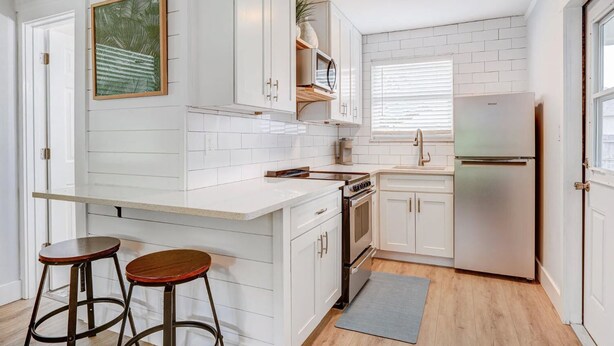 A compact kitchen with white cabinetry, a built-in oven, a refrigerator, and a bar stool. - Charming cottage in delightful Stuart with AC, WiFi (Stuart)