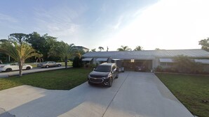 A residential driveway with a parked SUV, a garage, and a house with a metal roof. - Charming cottage in delightful Stuart with AC, WiFi (Stuart)