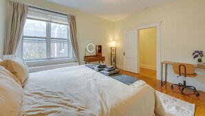 Une chambre à coucher avec un grand lit, un bureau, une chaise, un miroir et une fenêtre avec des rideaux.
