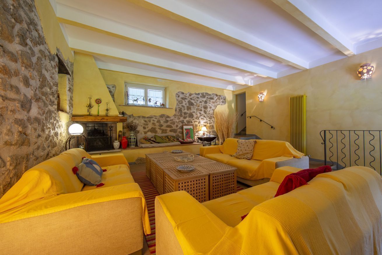 A cozy living room with yellow sofas, a fireplace, stone walls, and a stone fireplace surround.