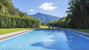 Una piscina amb vistes a les muntanyes, envoltada d'arbres i una zona verda.